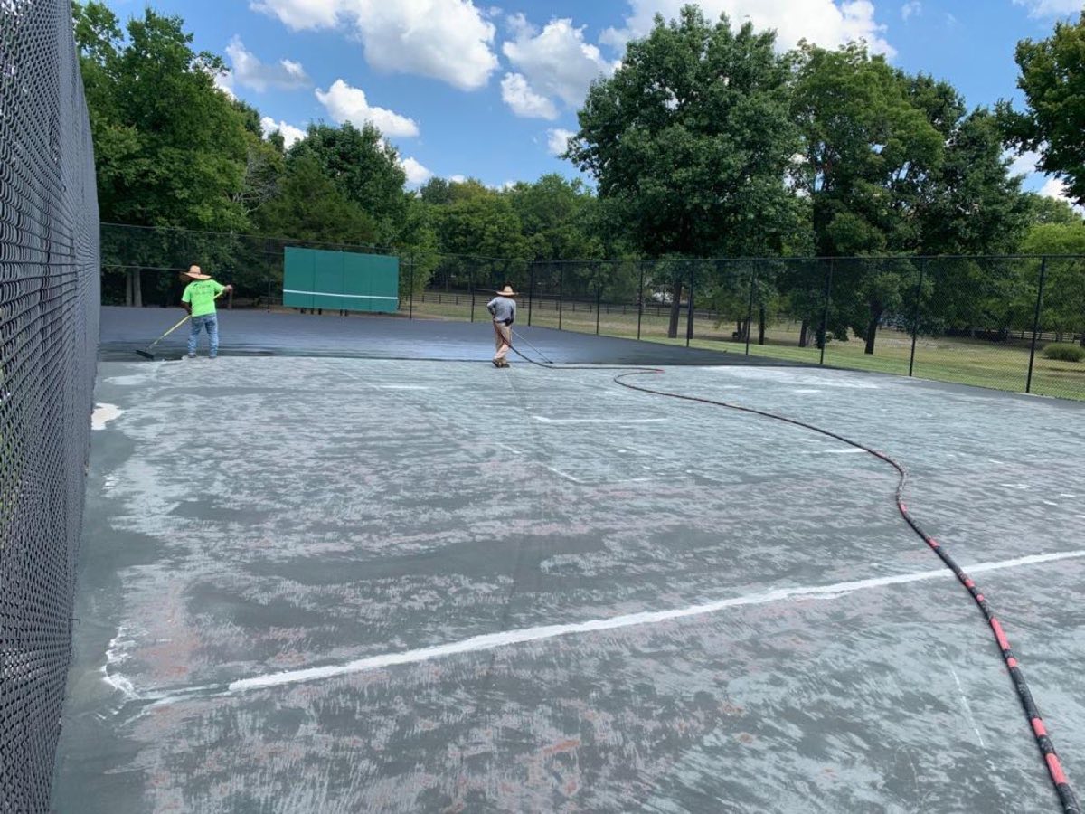 Crew squeegeeing resurfacer across the court